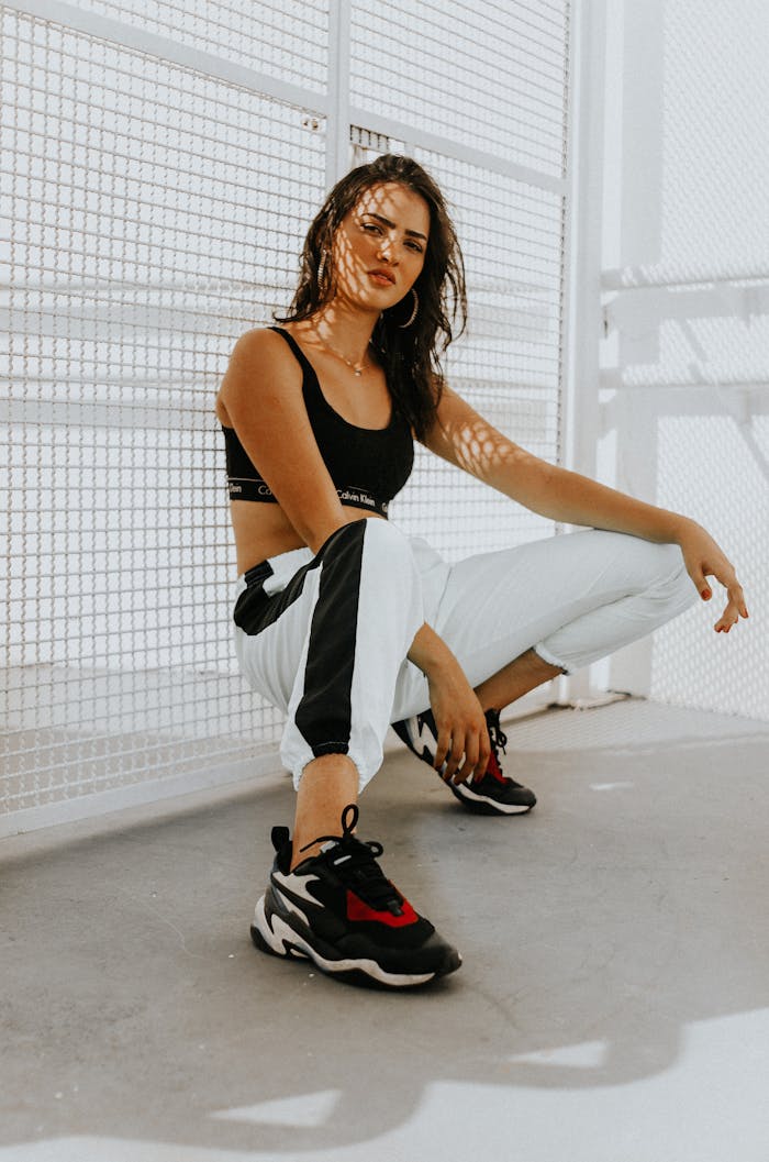 about-07 Confident woman in urban attire, featuring trendy sneakers, crouching in sunlight.