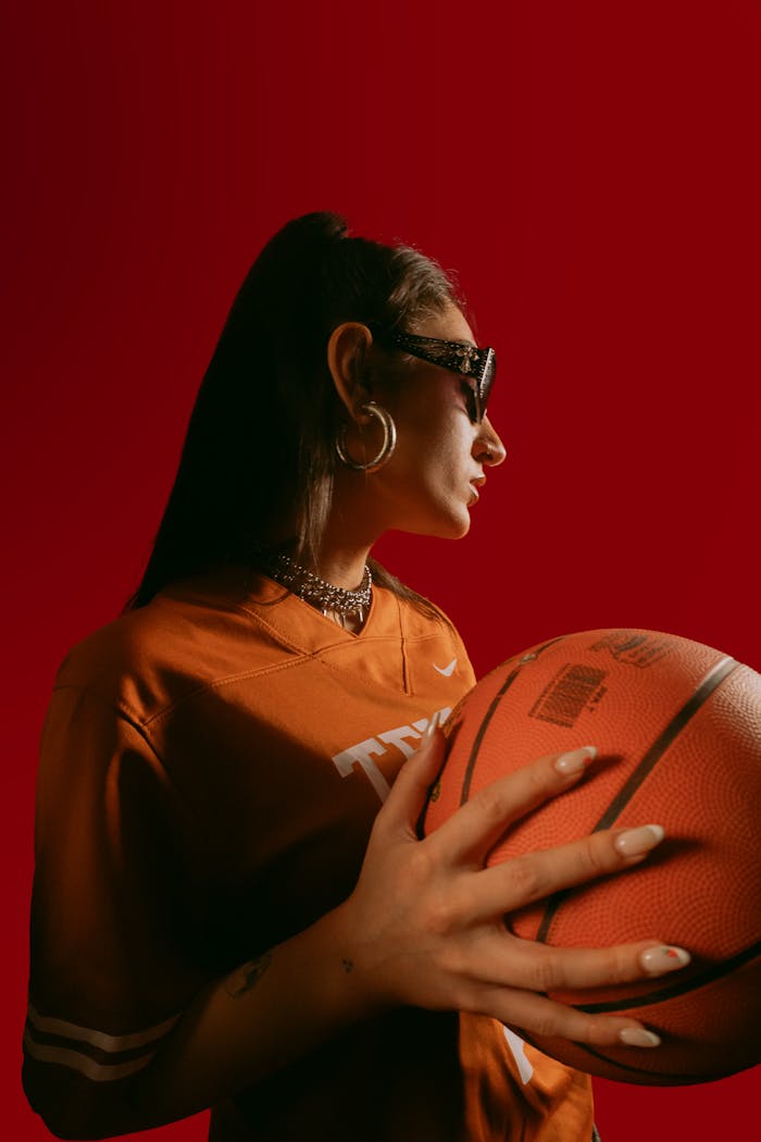 our-story-01 Profile of a fashionable woman with sunglasses holding a basketball, set against a vibrant red backdrop.