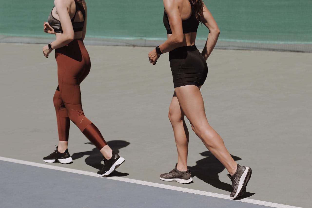 mission-02 Two women walking on an outdoor track in sportswear, emphasizing healthy lifestyle and fitness.